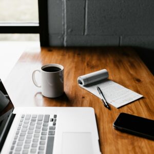 A tidy workspace featuring a laptop, coffee cup, phone, and notepad on a wooden desk.